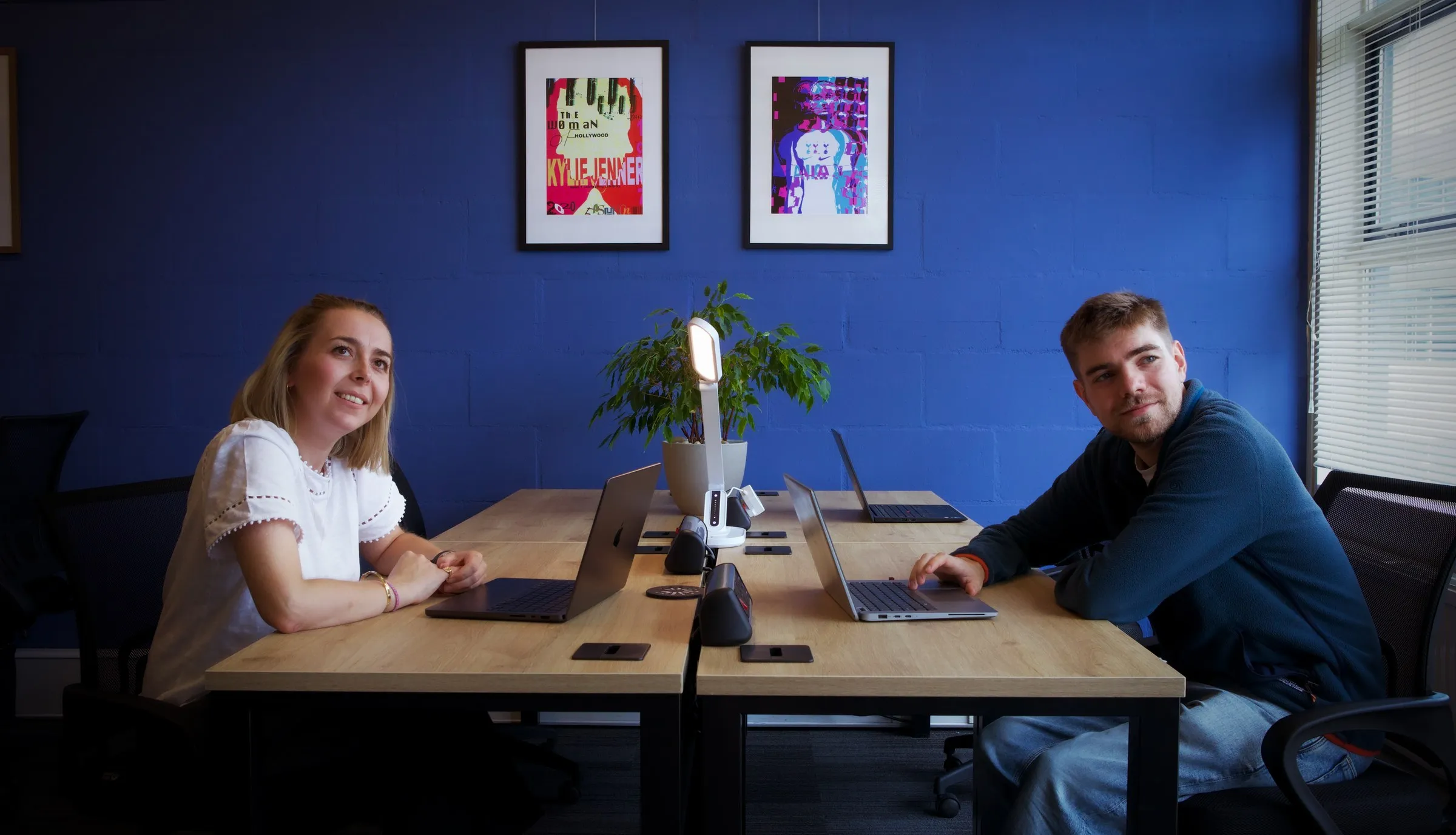 Two founders at a shared desk against the Studio's blue wall