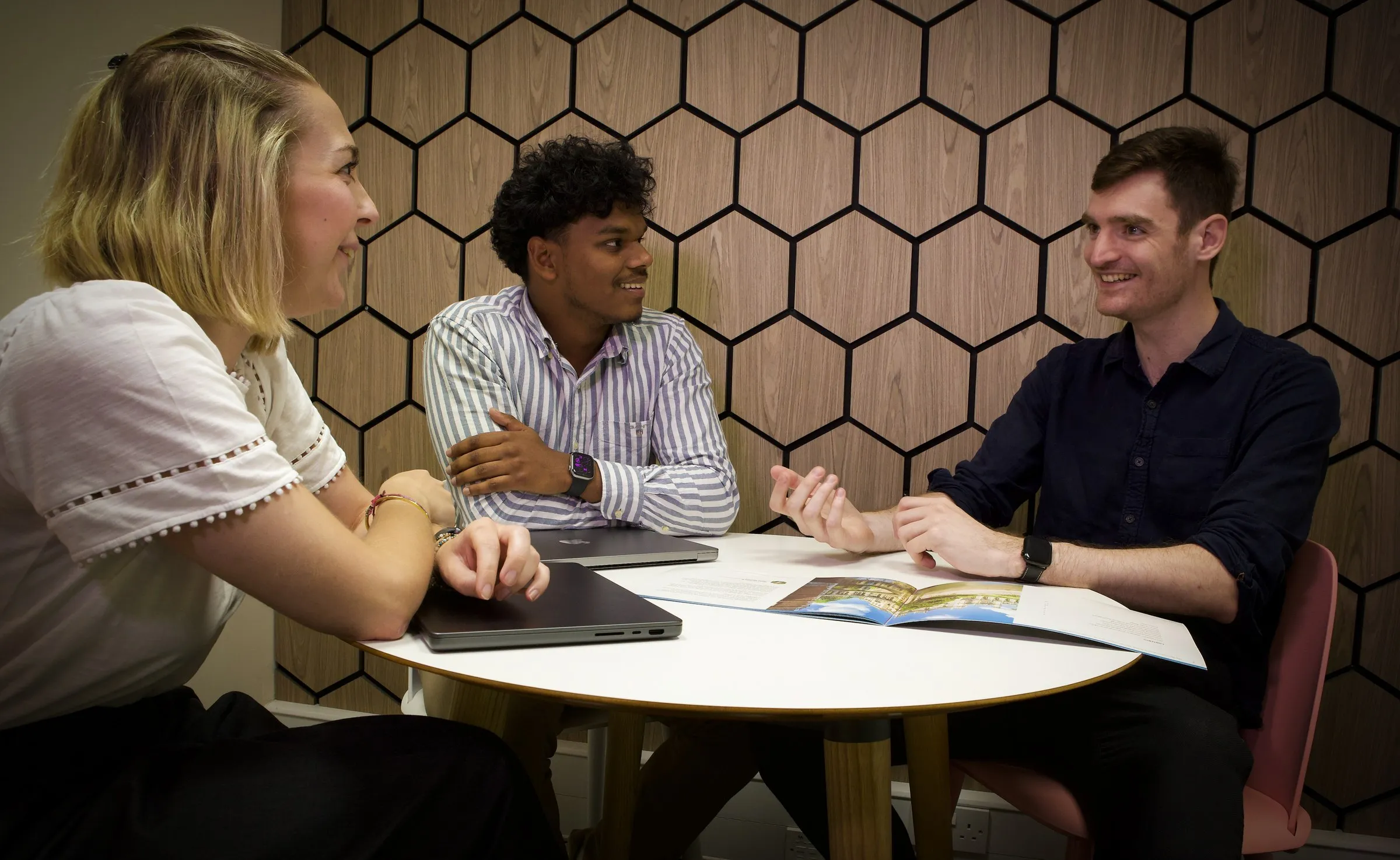 Three members around a table in front of the hexagon wall